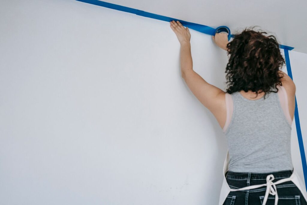 Vrouw brengt blauwe afplaktape aan op een muur